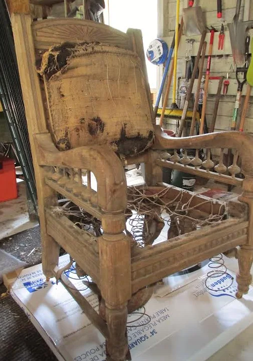 Antique Eastlake armchair stripped to the bare oak frame with torn burlap and exposed coil springs in the workshop
